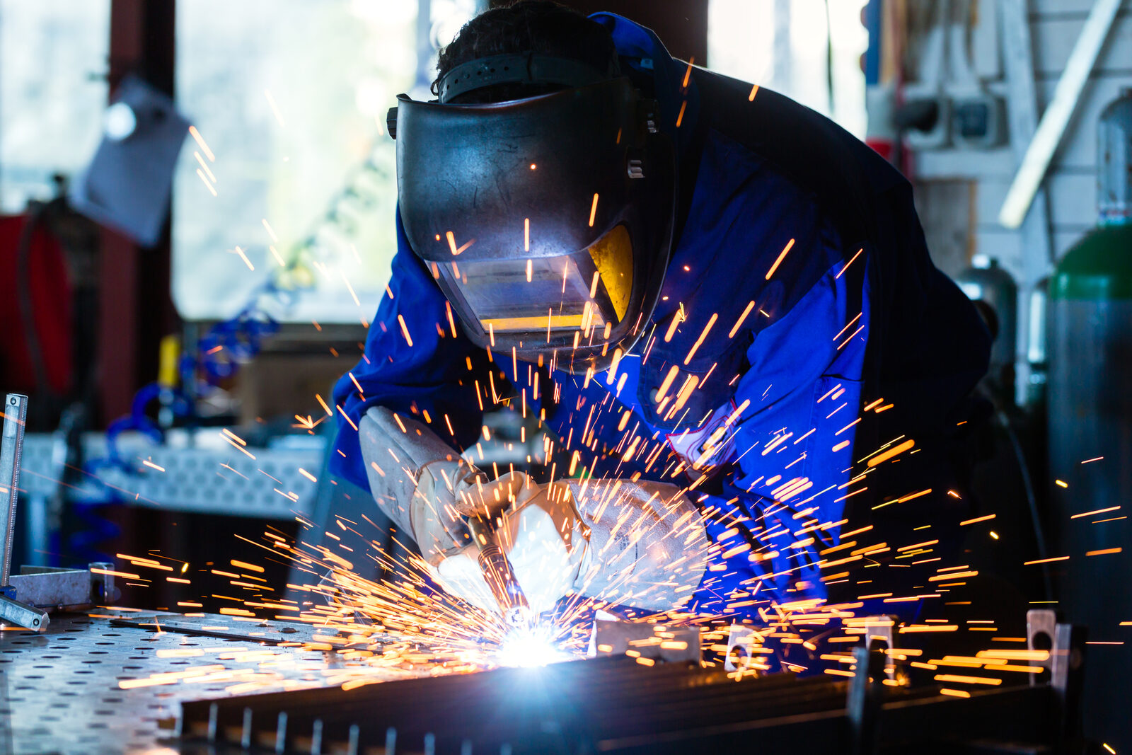 A welder joining metal with sparks flying, face shielded behind goggles